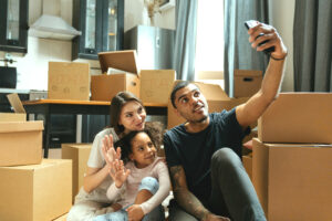 Man, woman and child sitting in a kitchen among packing boxes. Taking a selfie.