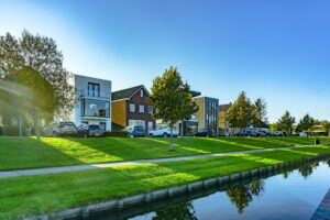 Residential housing in the Netherlands. Parked cars and grass leading to the water's edge in the foreground.