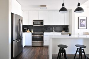 Modern kitchen with white units, silver fridge freezer and a breakfast bar with two black stools.