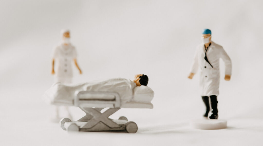Toy figurines: Patient on a hospital bed. Doctor and nurse in the background.