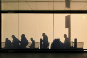 Silhouettes of passengers at an airport, behind a glass screen.